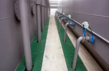 Green FRP grating installed around chemical storage tanks and industrial piping